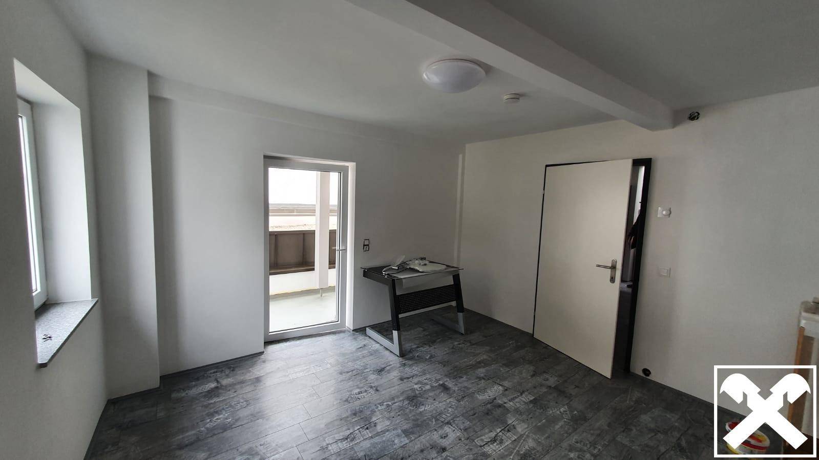 Heller Wohnraum mit Zugang zu einem Balkon und dunklem Laminatboden, bietet viel natürliches Licht.