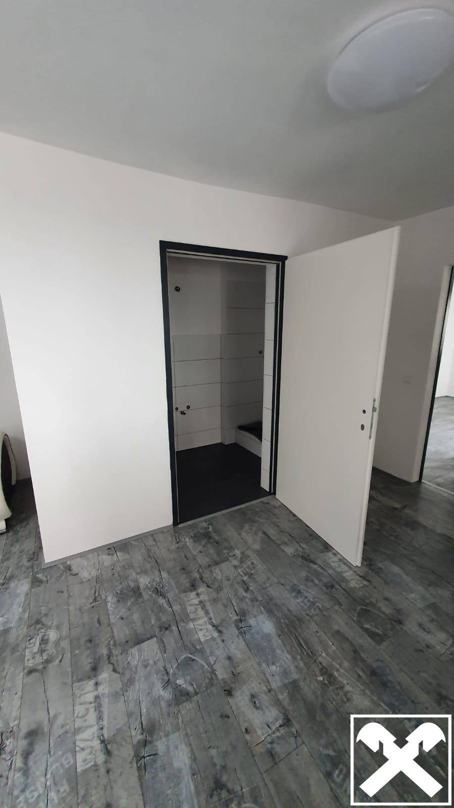 Offene Tür zu einem Badezimmer mit dunklen Fliesen und Duschbereich, modern gestaltet.
