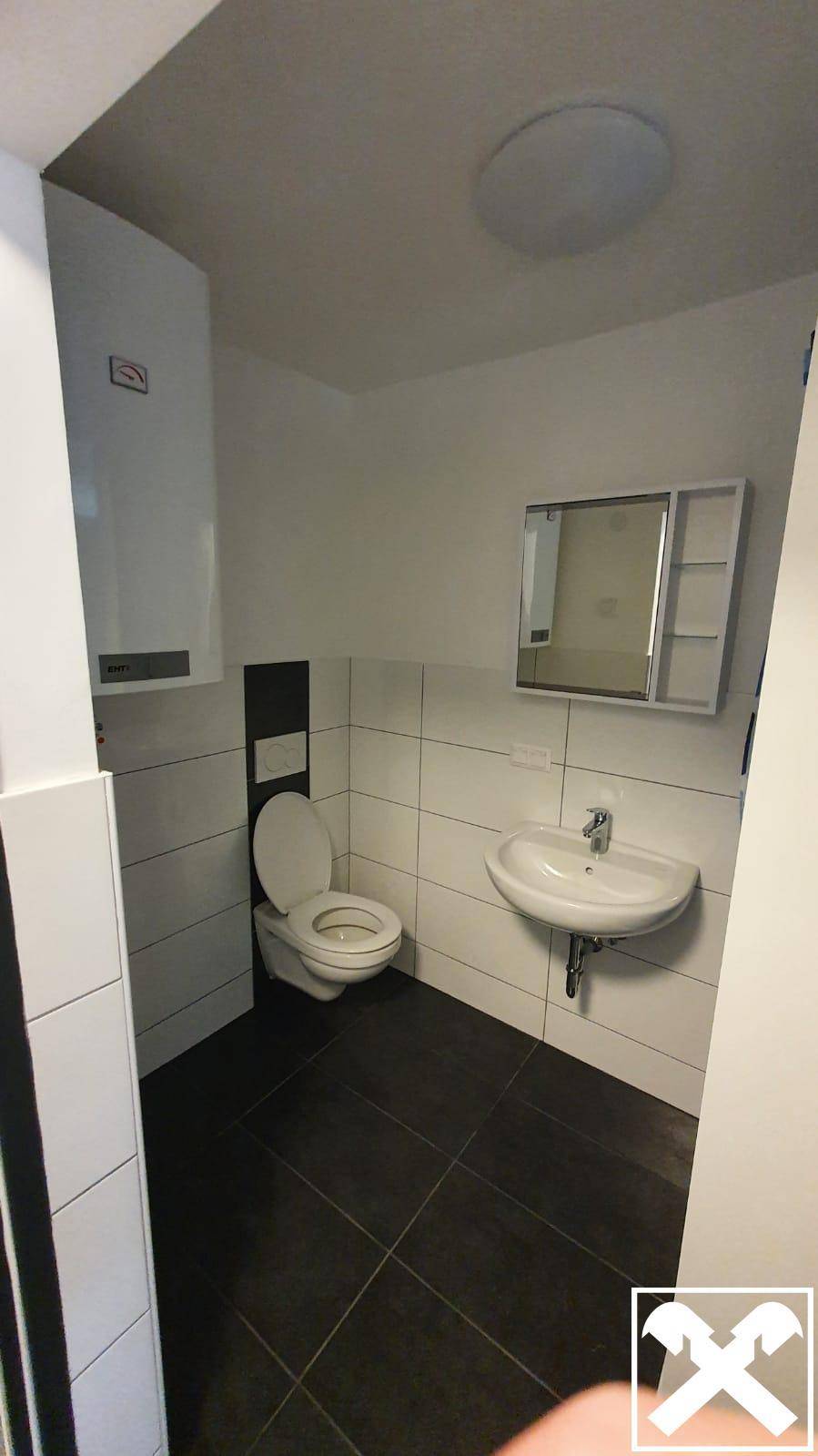 Kleines WC mit Waschbecken, Spiegelschrank und dunklen Bodenfliesen, sauber und funktional.