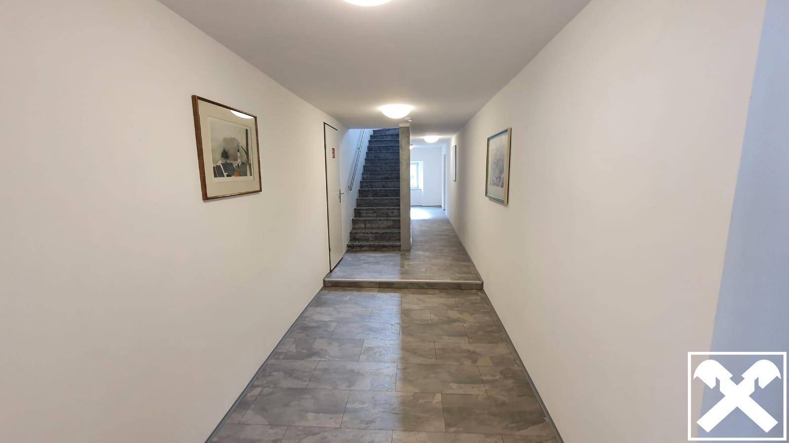 Langer Flur mit hellen Wänden, Fliesenboden und Zugang zu verschiedenen Wohnungen im Gebäude.