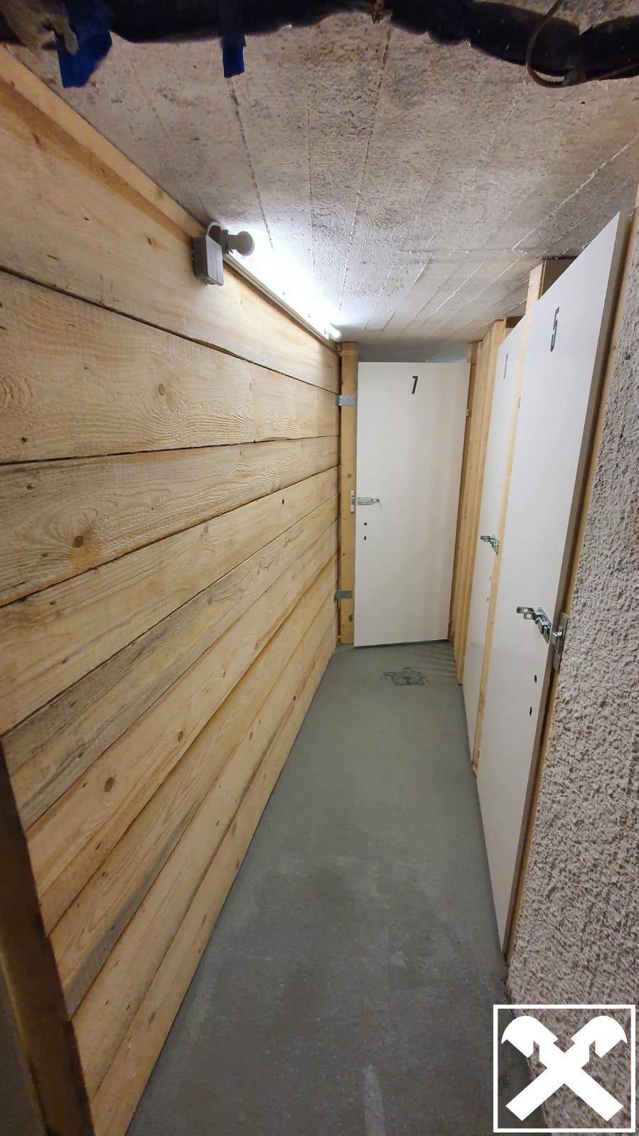 Abstellräume mit Holzwänden und nummerierten Türen im Kellerbereich, bieten viel Stauraum.
