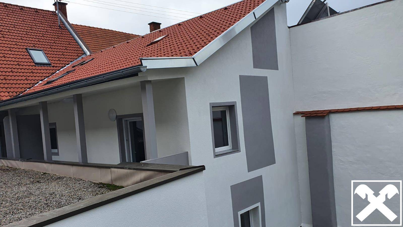 Seitenansicht eines Gebäudes mit weißer Fassade, grauen Akzenten und Ziegeldach unter bewölktem Himmel.