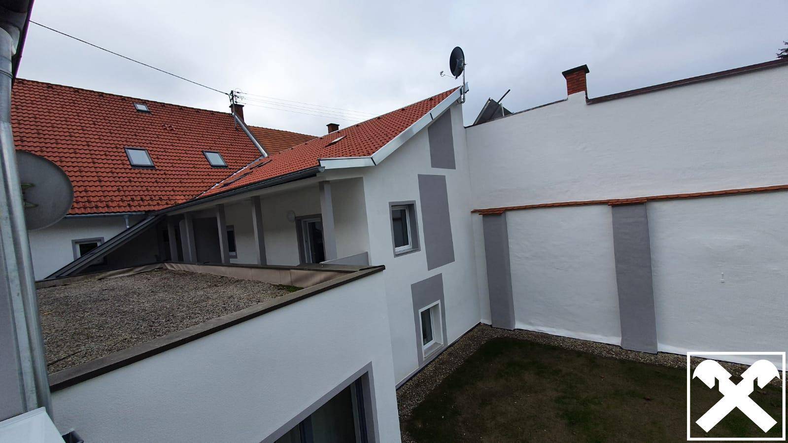 Rückansicht eines Gebäudes mit Ziegeldach, weißer Fassade und kleinem Rasenbereich im Garten.