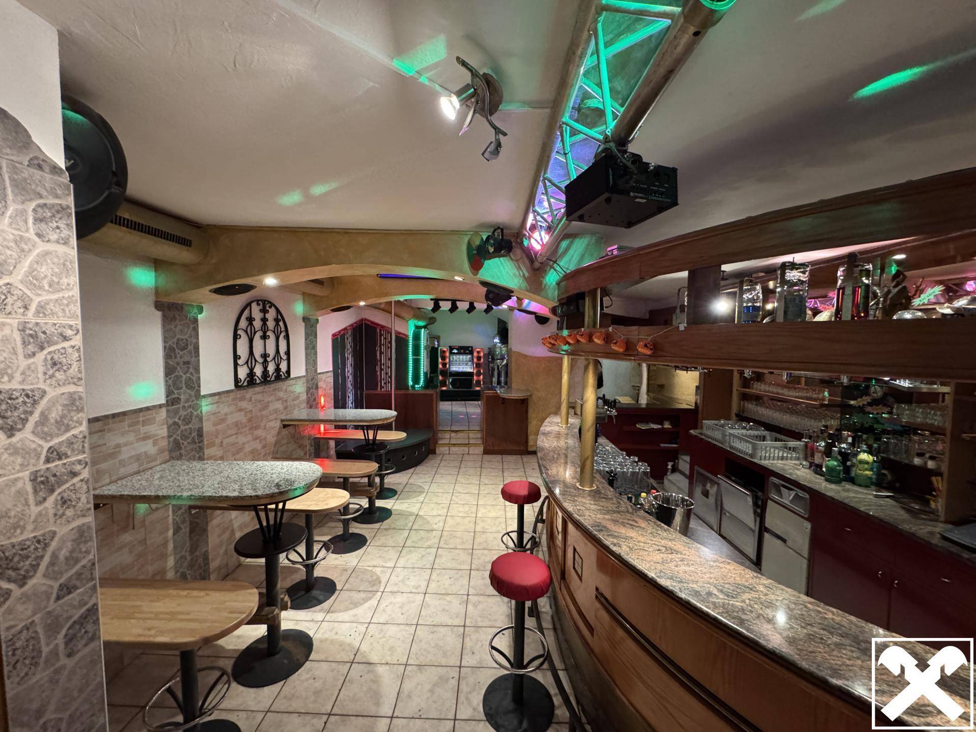 Innenansicht einer Bar mit Theke, Sitzgelegenheiten und farbiger Beleuchtung, einladende Atmosphäre.