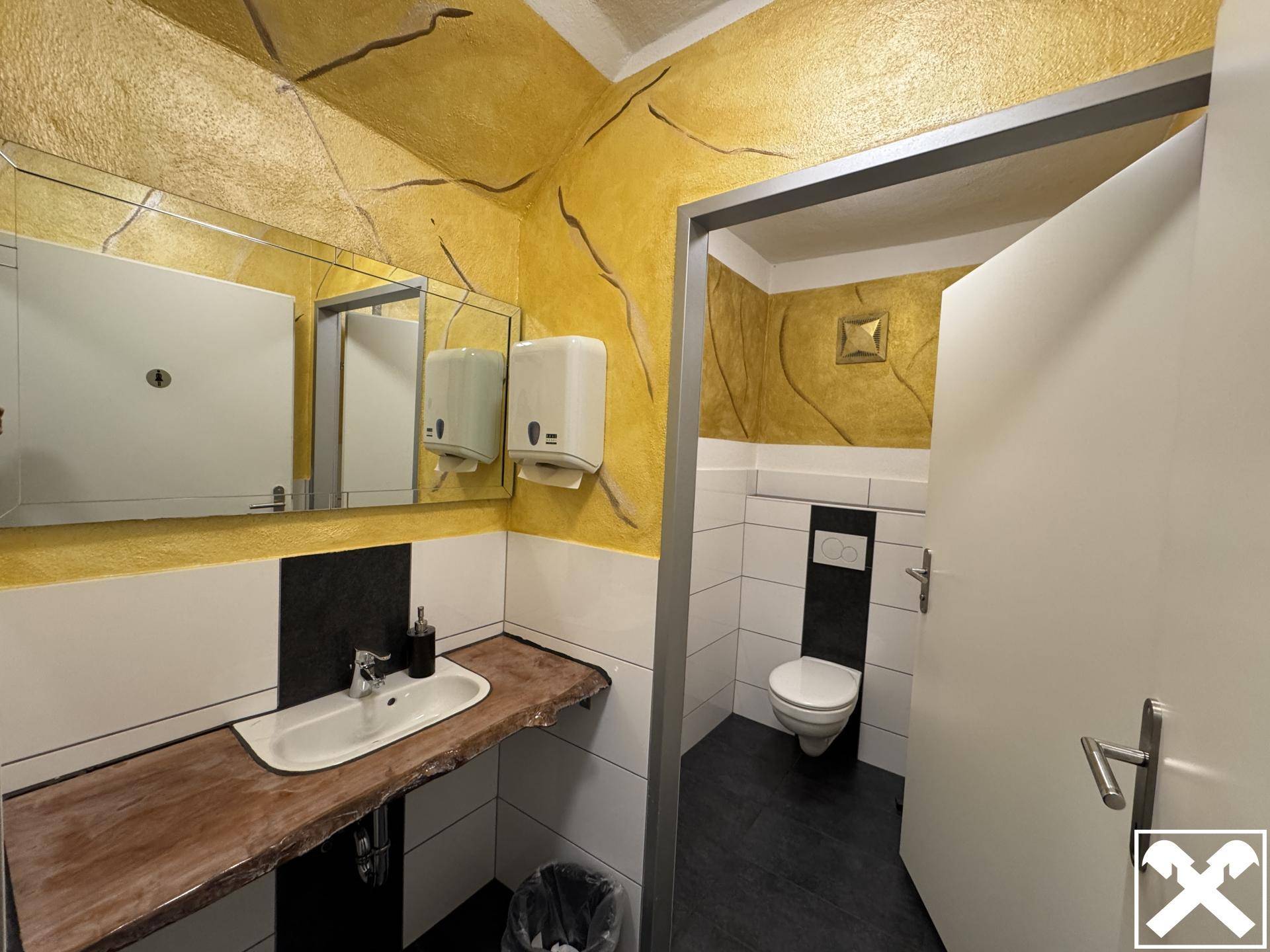 Modernes WC mit Waschbecken, Spiegeln und auffälliger gelber Wandgestaltung, sauber und hell.
