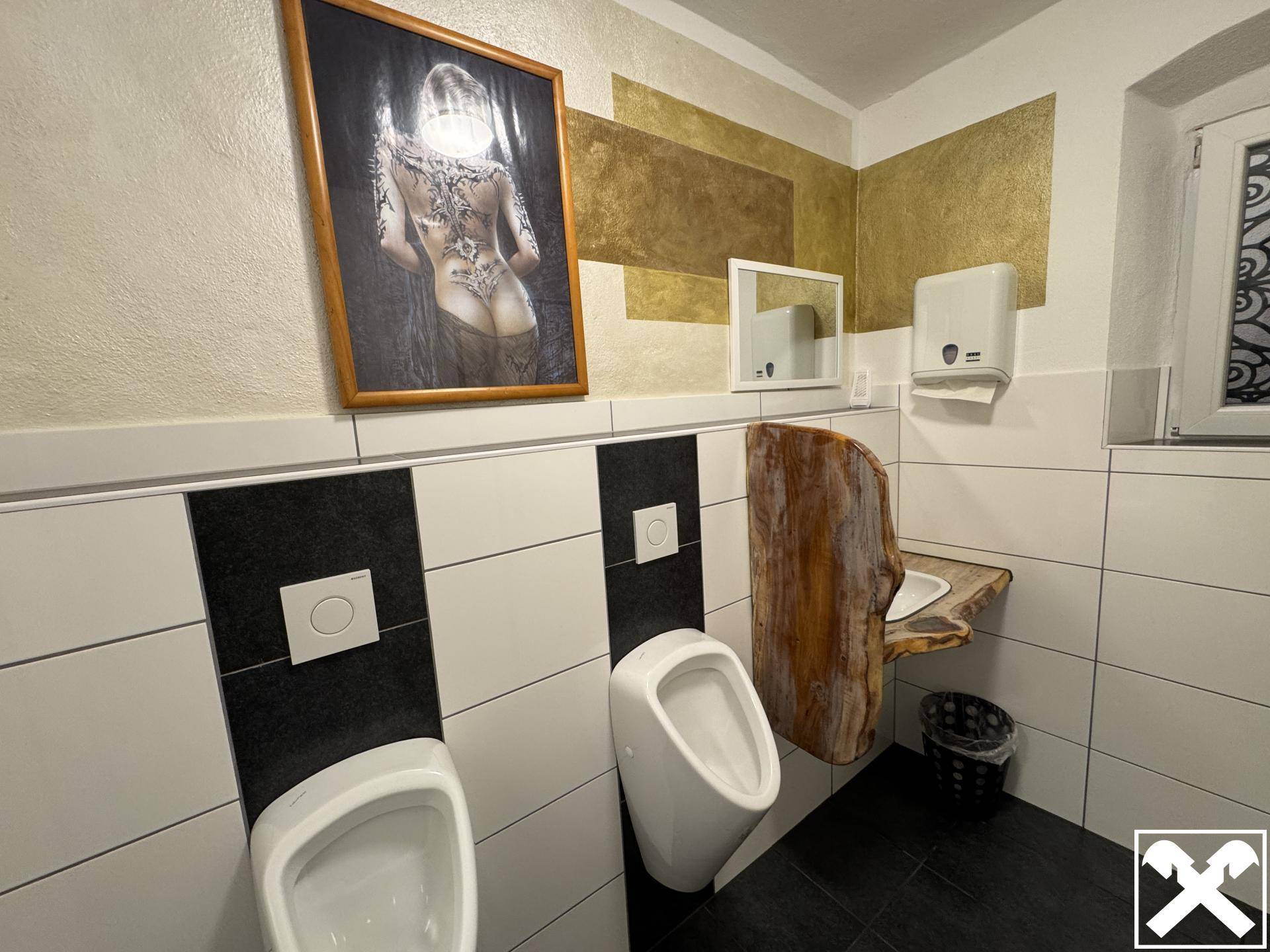 Herren-WC mit Urinalen, Waschbecken und einer einzigartigen Holzplatte als Waschtisch, modern gestaltet.