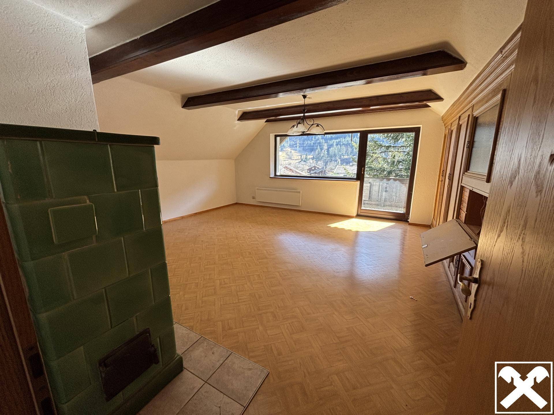 Geräumiges Wohnzimmer mit Holzbalken, Laminatboden und Kachelofen mit Bergblick.