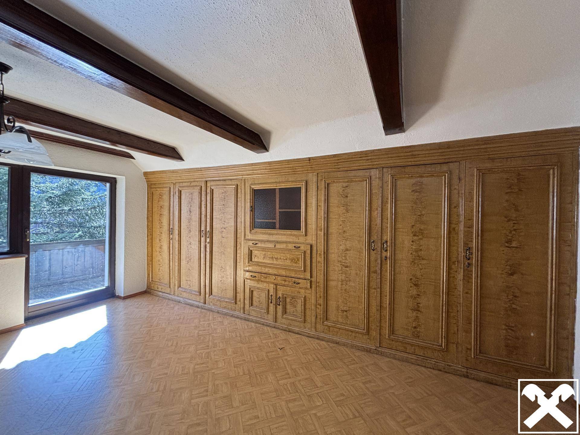 Wohnzimmer mit großer Einbauschrankwand aus Holz und Zugang zum Balkon.