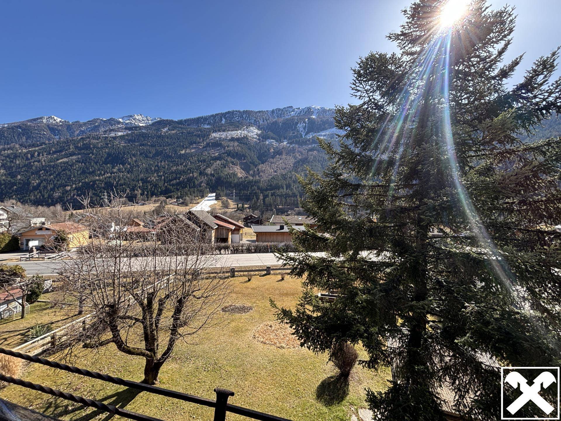 Sonniger Bergblick von einem Balkon auf die umliegende Landschaft und Bäume.