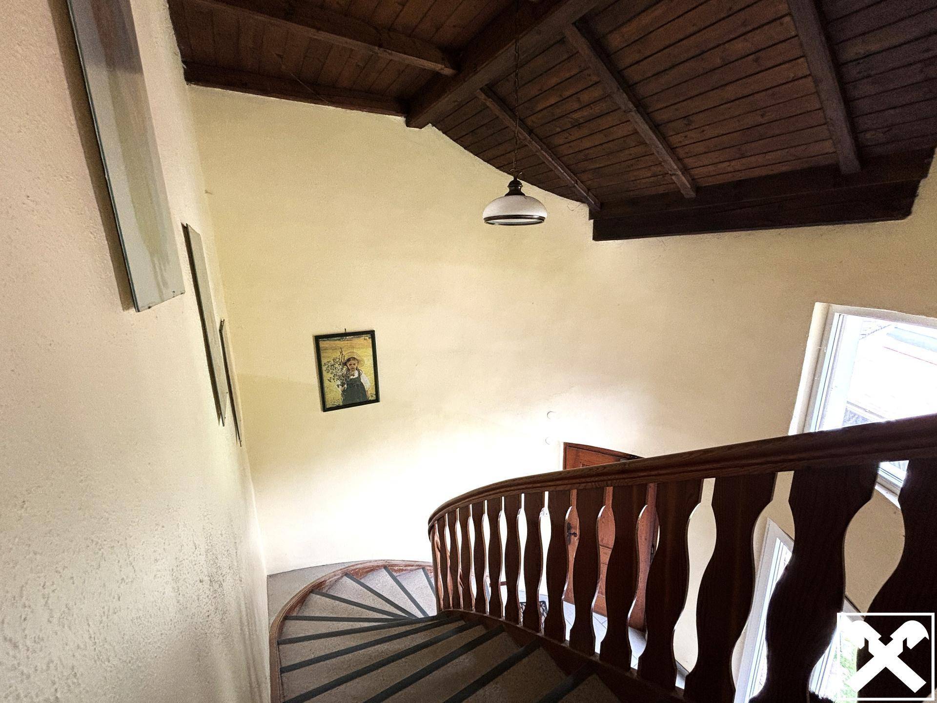 Geschwungene Holztreppe mit Holzbalkendecke und traditioneller Beleuchtung.