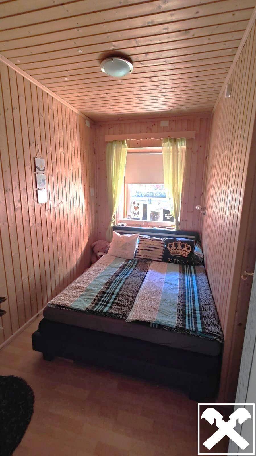 Kleines Schlafzimmer mit Holztäfelung, Bett und Fenster.