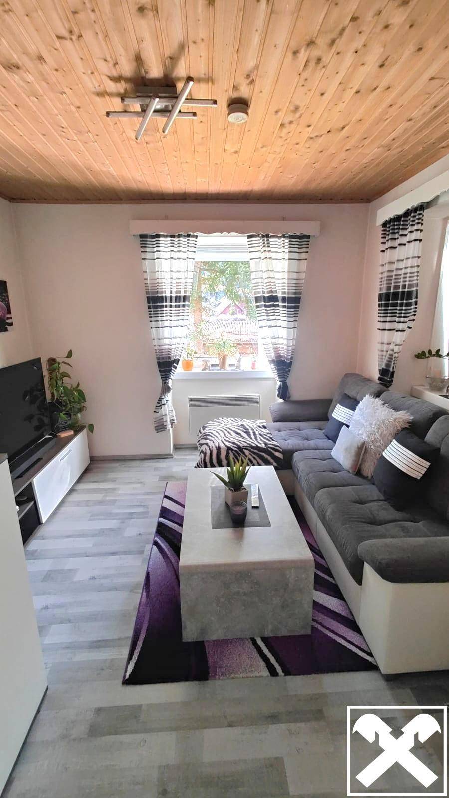Modern eingerichtetes Wohnzimmer mit L-förmigem Sofa, Teppich und Holzdecke.