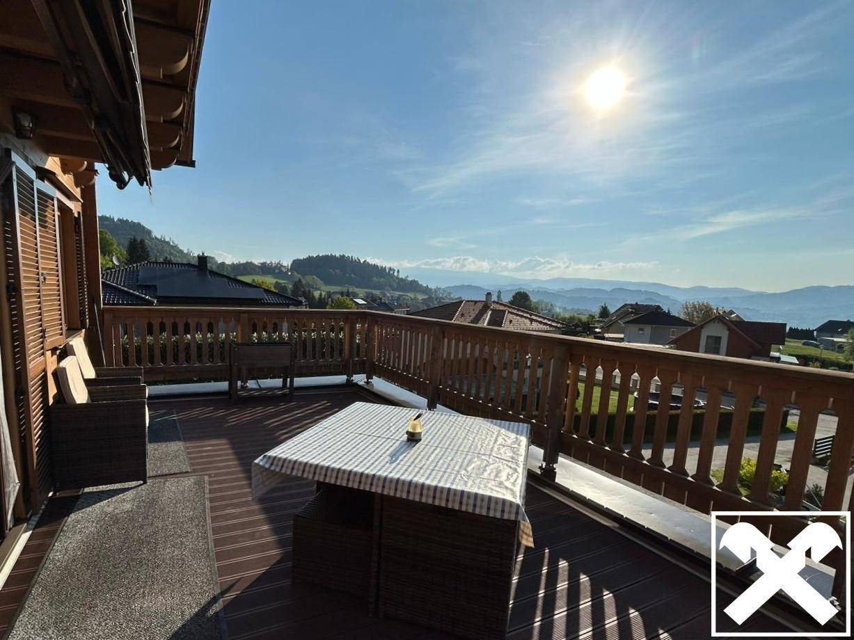Sonnige Terrasse mit Holzboden, Sitzgelegenheiten und weitem Blick auf die Berge.