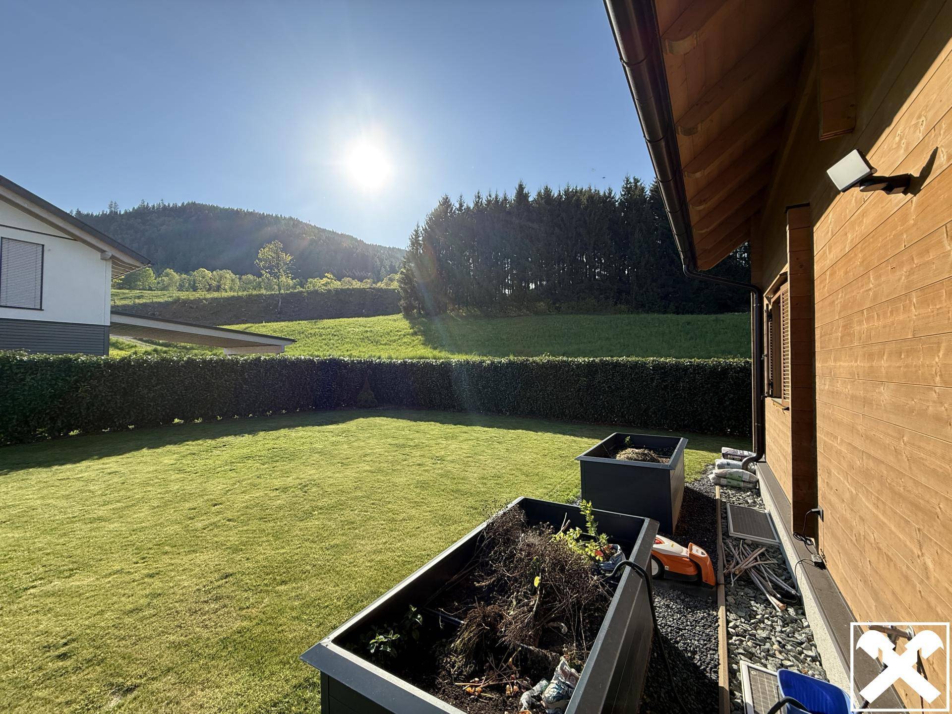 Gepflegter Gartenbereich mit Rasenfläche und Hochbeeten, umgeben von Hecken und Bäumen.