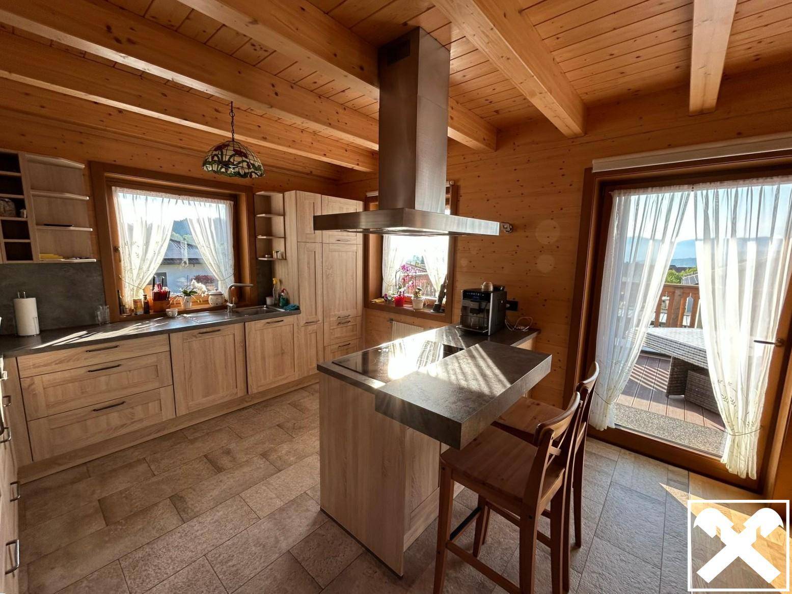 Moderne Holzküche mit Kochinsel, Dunstabzugshaube und Zugang zur Terrasse.
