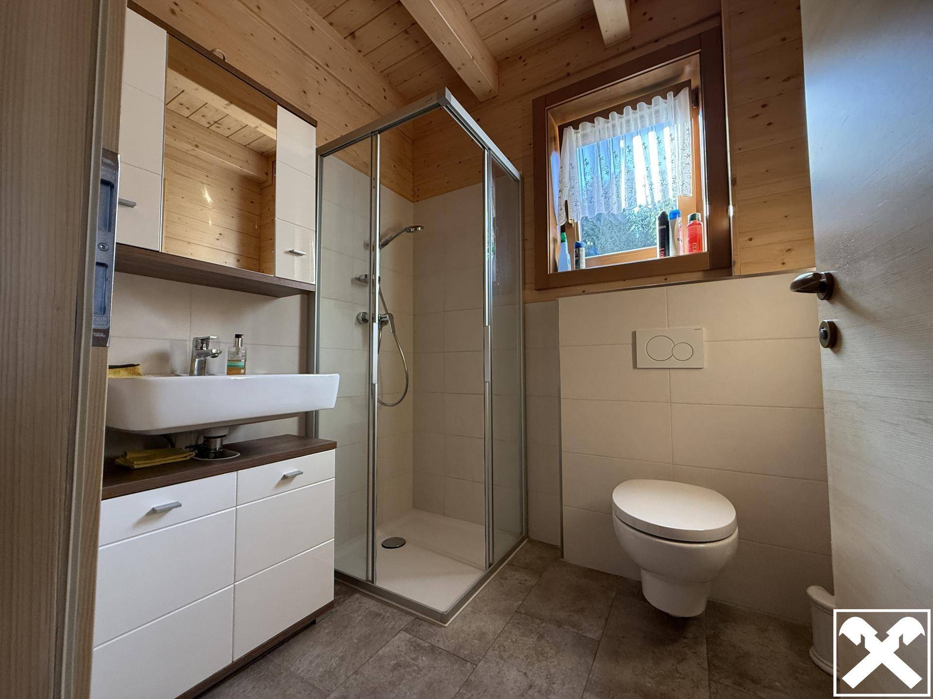 Modernes Badezimmer mit Dusche, Waschbecken und WC, hell gefliest und mit Holzdetails.