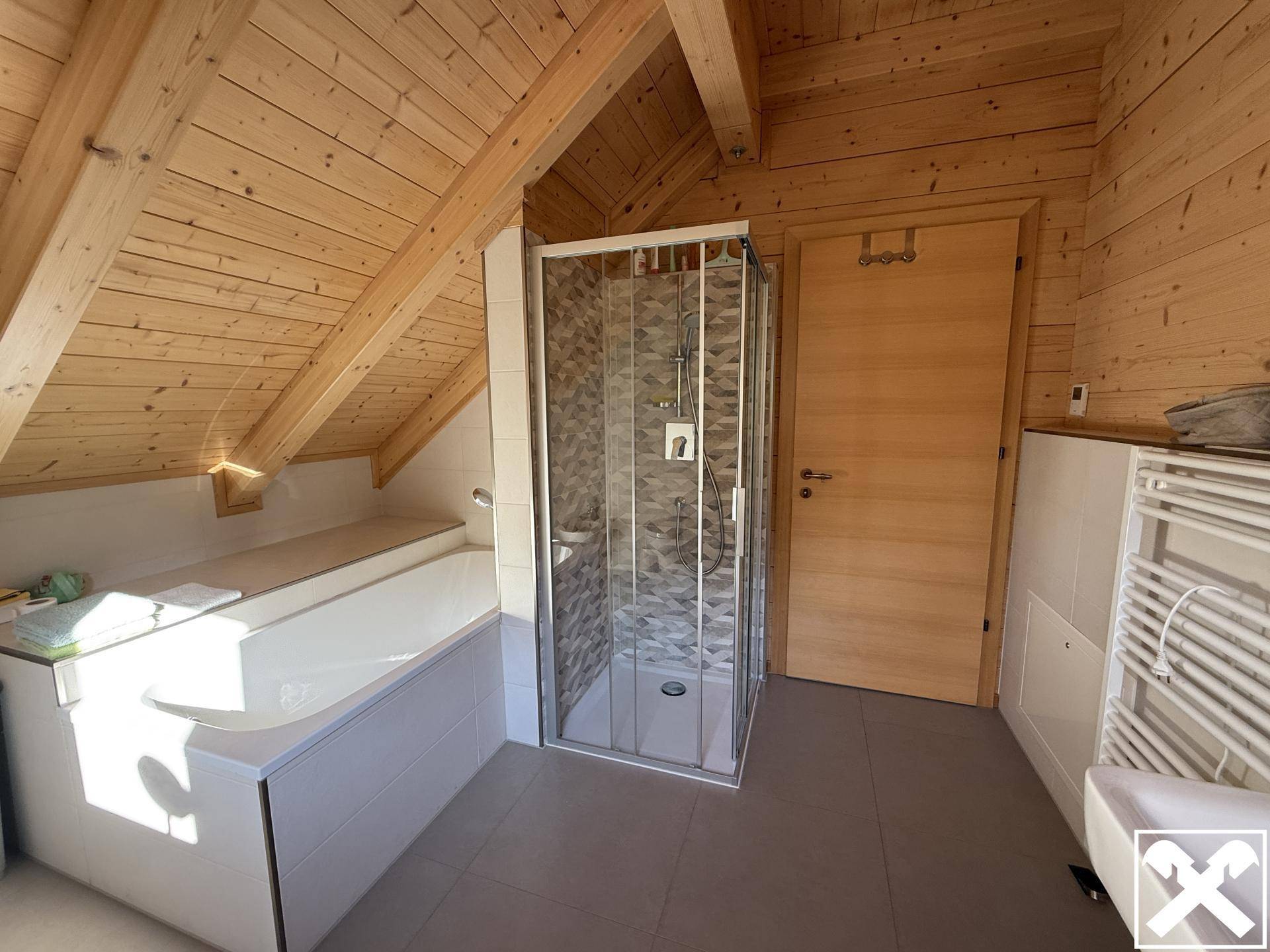 Dachgeschoss-Badezimmer mit Badewanne, Dusche und schrägen Holzdachschrägen.