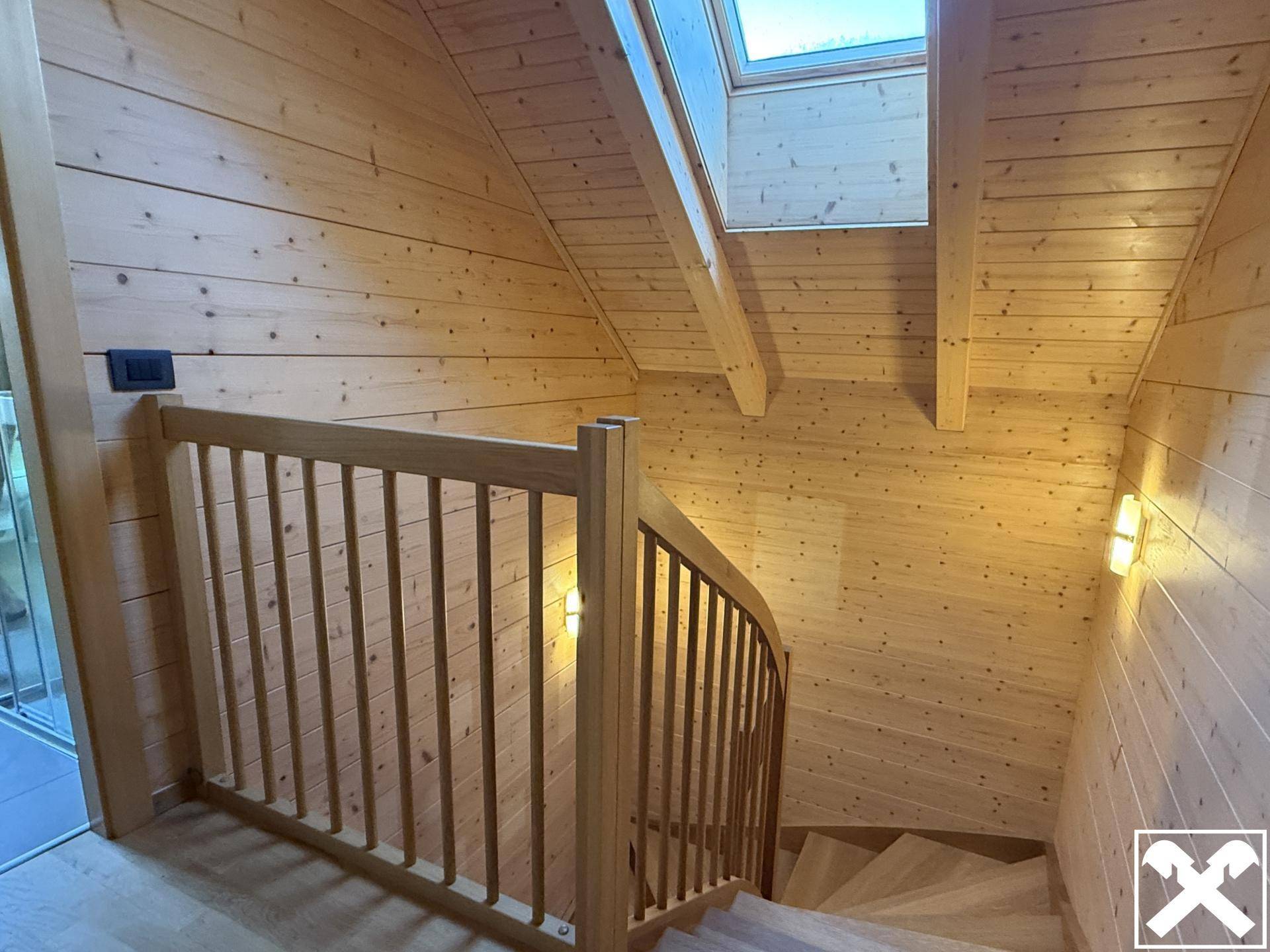 Heller Treppenaufgang mit Holzvertäfelung und Dachfenster für natürliches Licht.