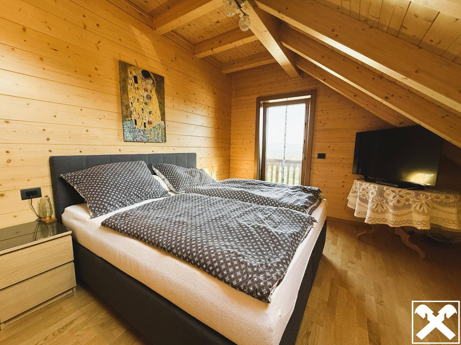 Helles Schlafzimmer im Dachgeschoss mit Doppelbett, Holzboden und Zugang zum Balkon.