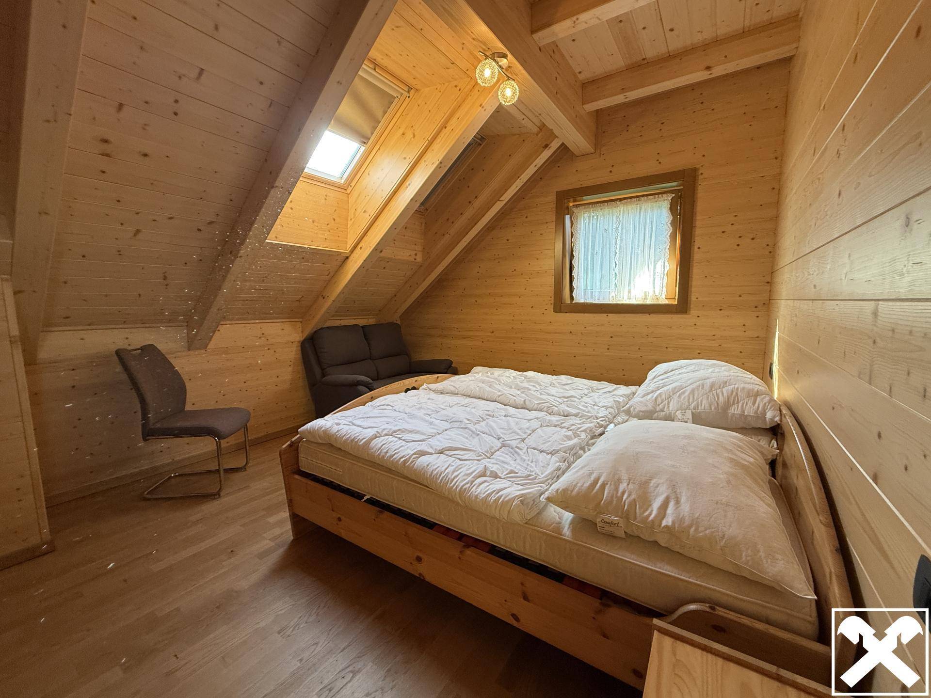 Gemütliches Schlafzimmer im Dachgeschoss mit Doppelbett, Holzvertäfelung und Dachfenster.
