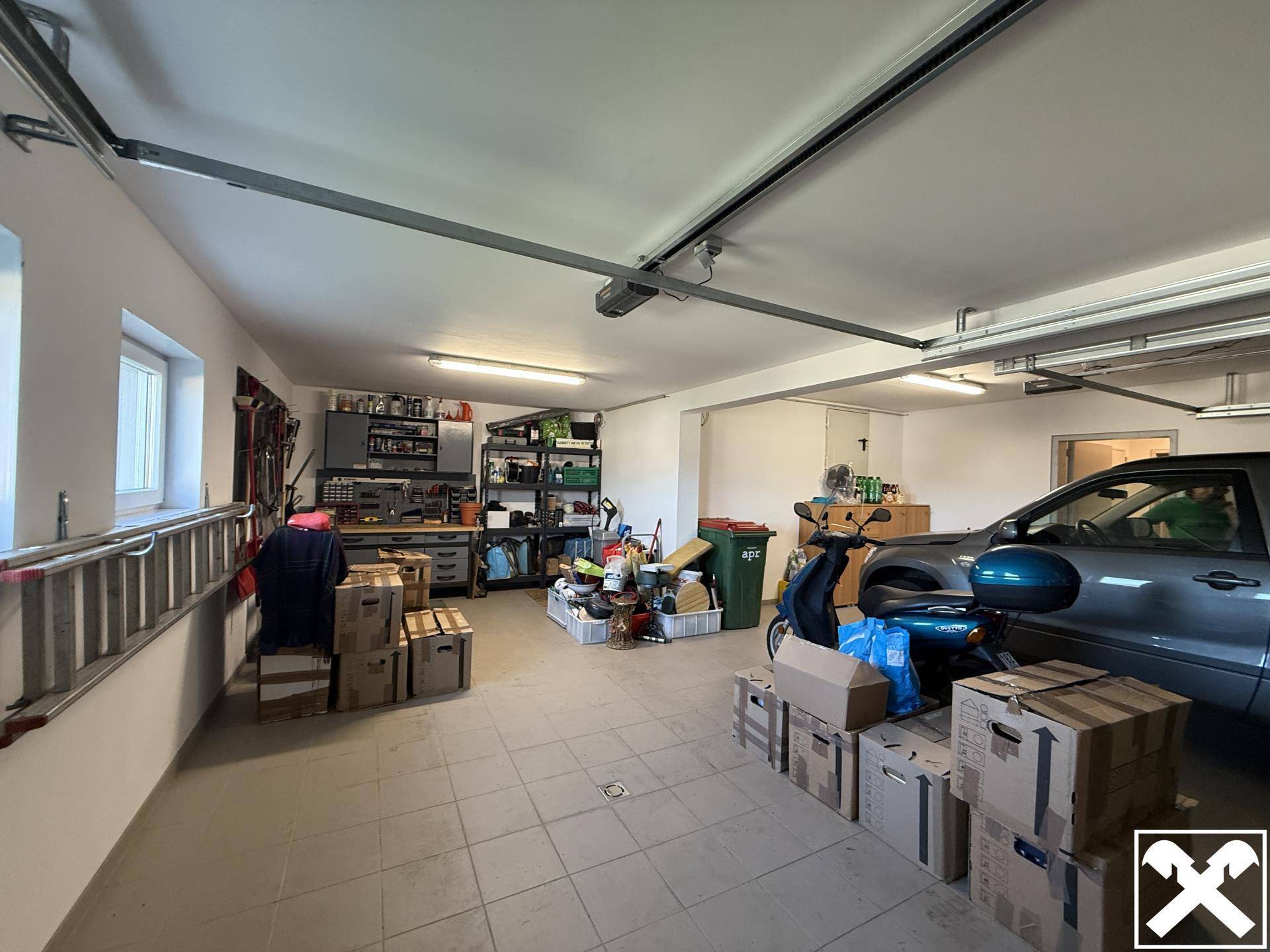 Geräumige Garage mit Fliesenboden, Werkstattbereich und Platz für Fahrzeuge.