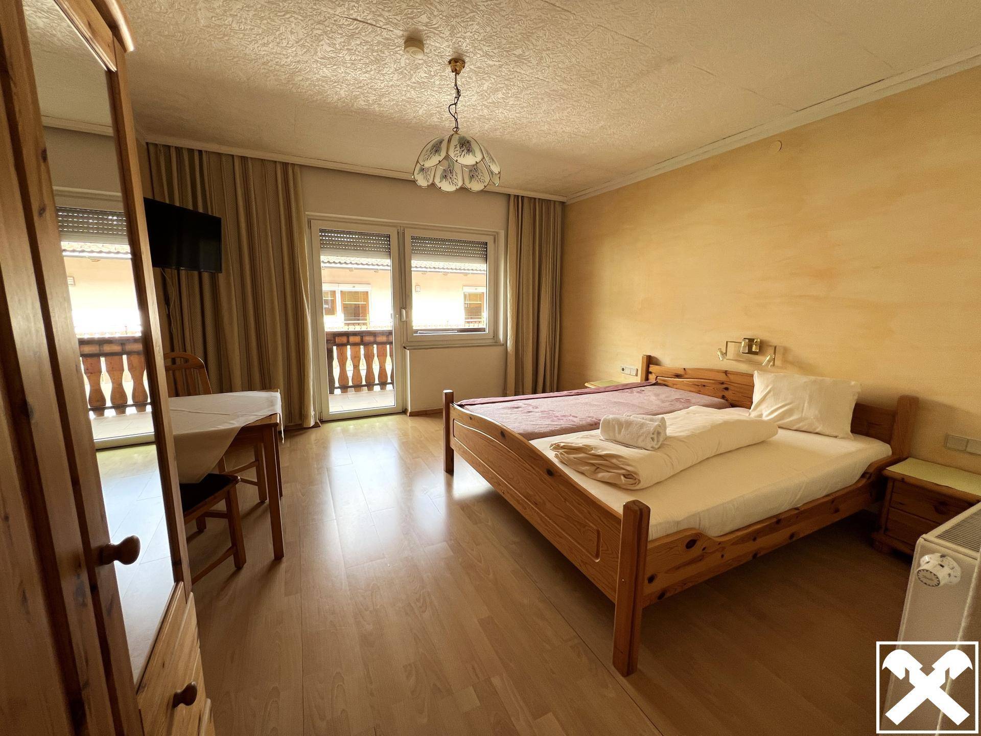 Helles Schlafzimmer mit Doppelbett, Holzboden und Zugang zu einem Balkon mit Bergblick.