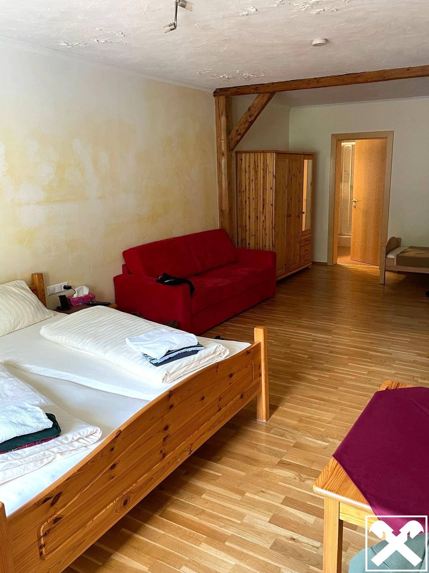 Geräumiges Schlafzimmer mit Holzboden, einem roten Sofa und sichtbaren Holzbalken an der Decke.