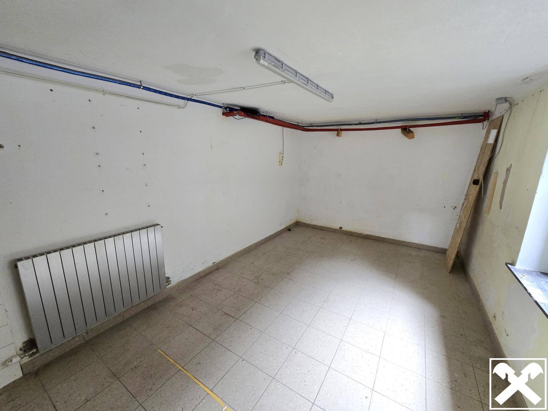 Einfacher Abstellraum oder Technikraum mit Fliesenboden, Heizkörper und sichtbaren Leitungen.