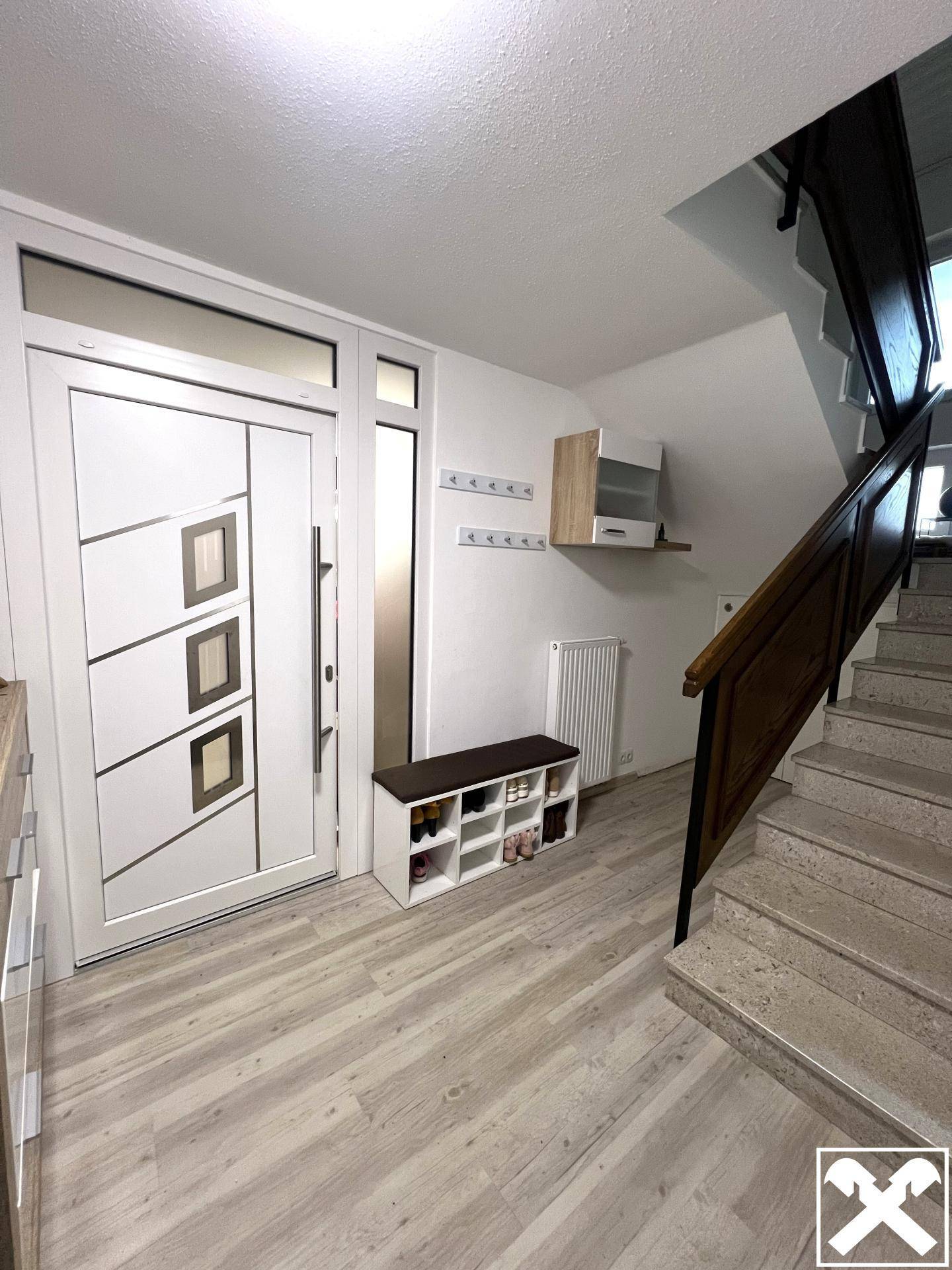 Heller Eingangsbereich mit moderner Haustür, Schuhregal und Treppe zum Obergeschoss.