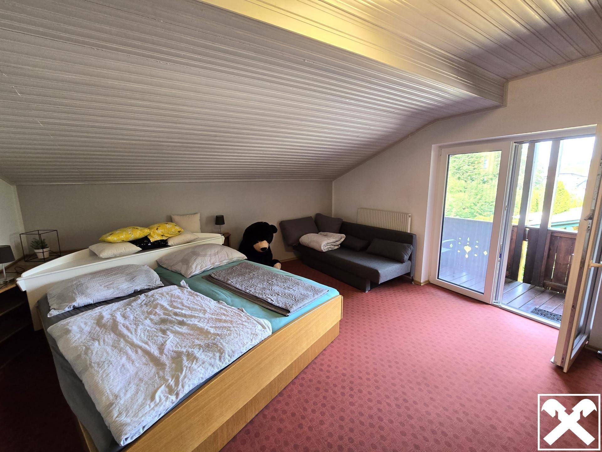 Schlafzimmer im Dachgeschoss mit Doppelbett, Sofa und Balkonzugang.