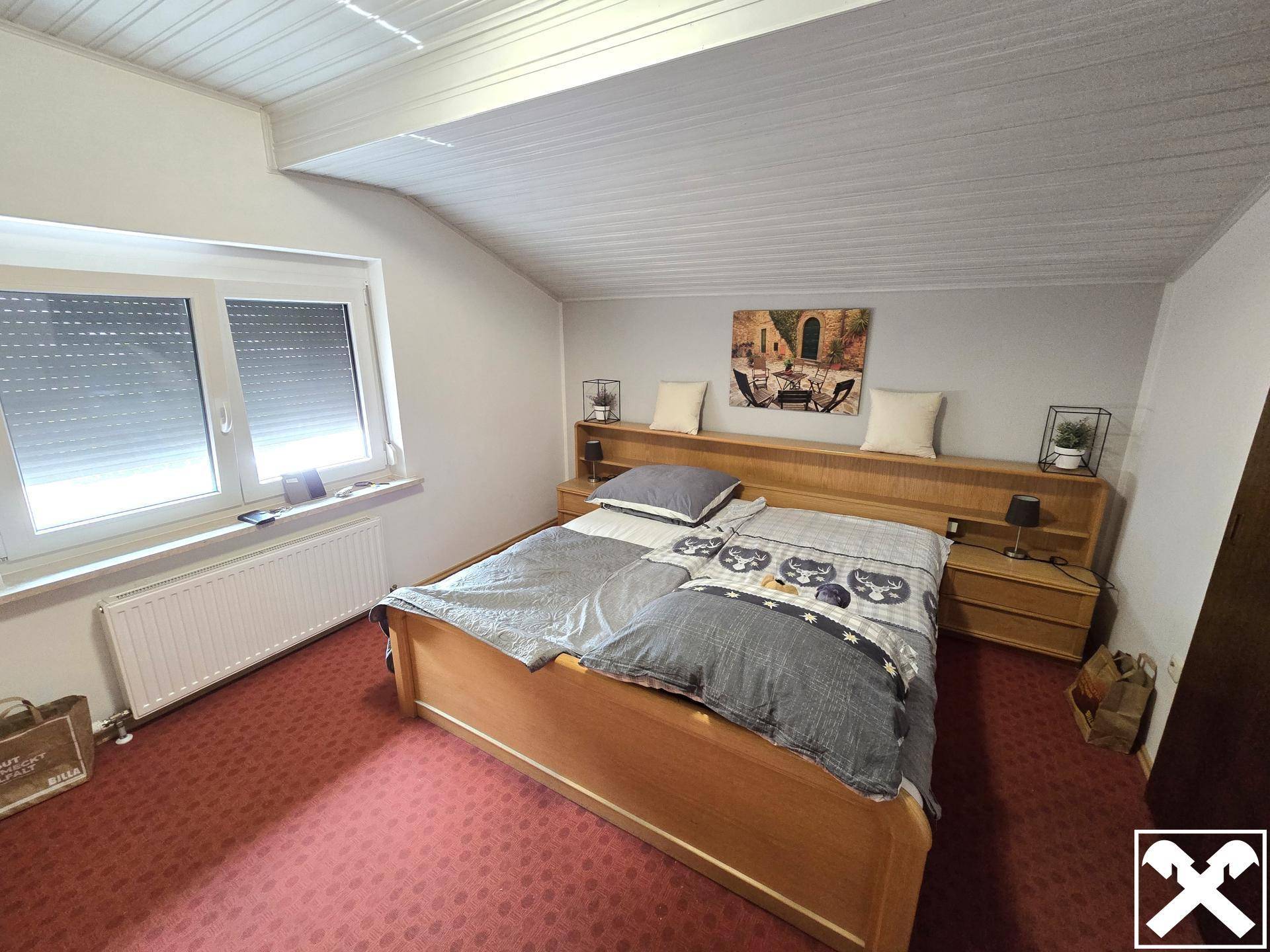 Gemütliches Schlafzimmer mit Doppelbett, Teppichboden und Dachschräge, ausgestattet mit Rollläden am Fenster.