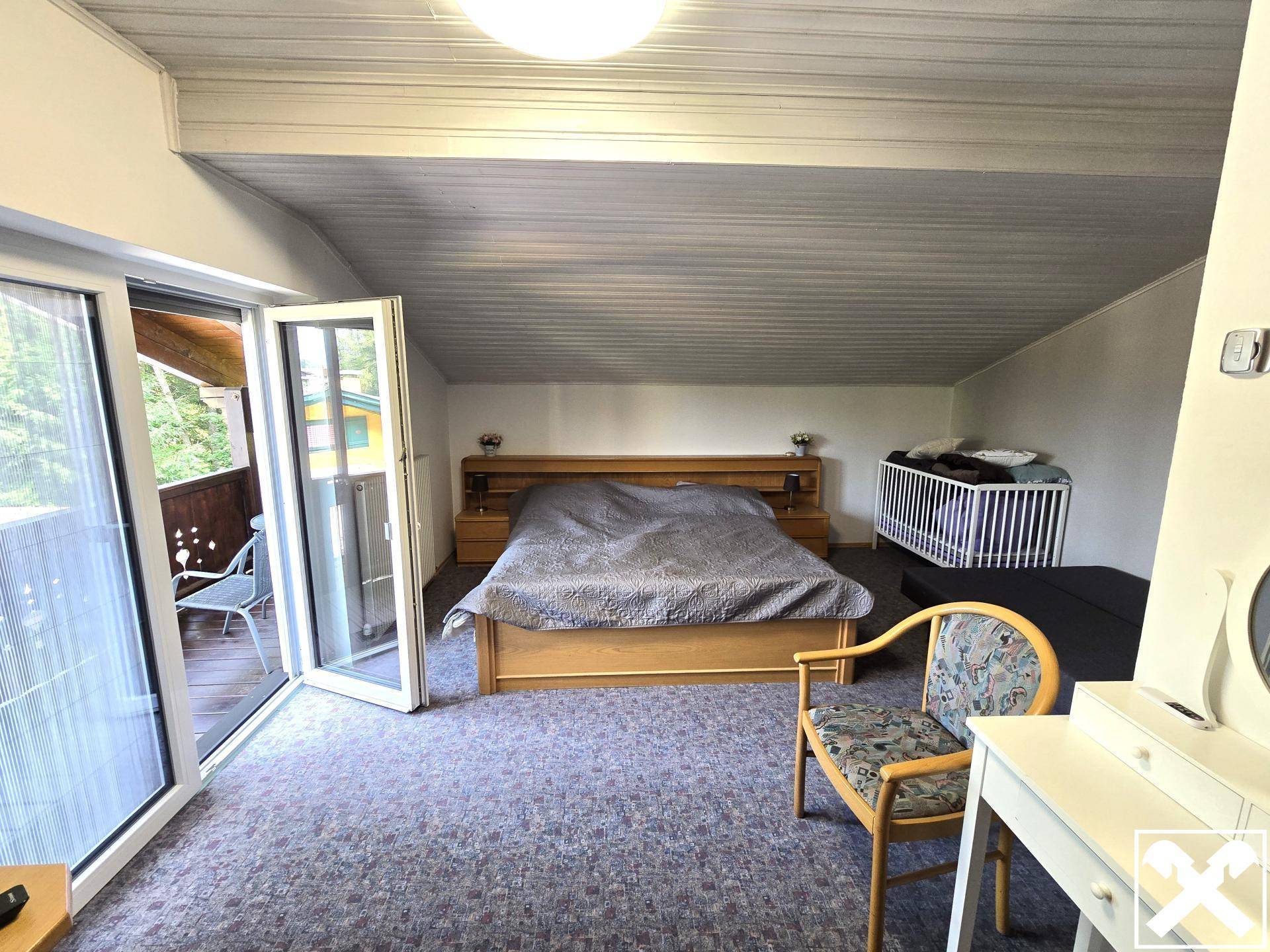 Helles Schlafzimmer mit Zugang zum Balkon, Teppichboden und Dachschräge, inklusive Babybett.