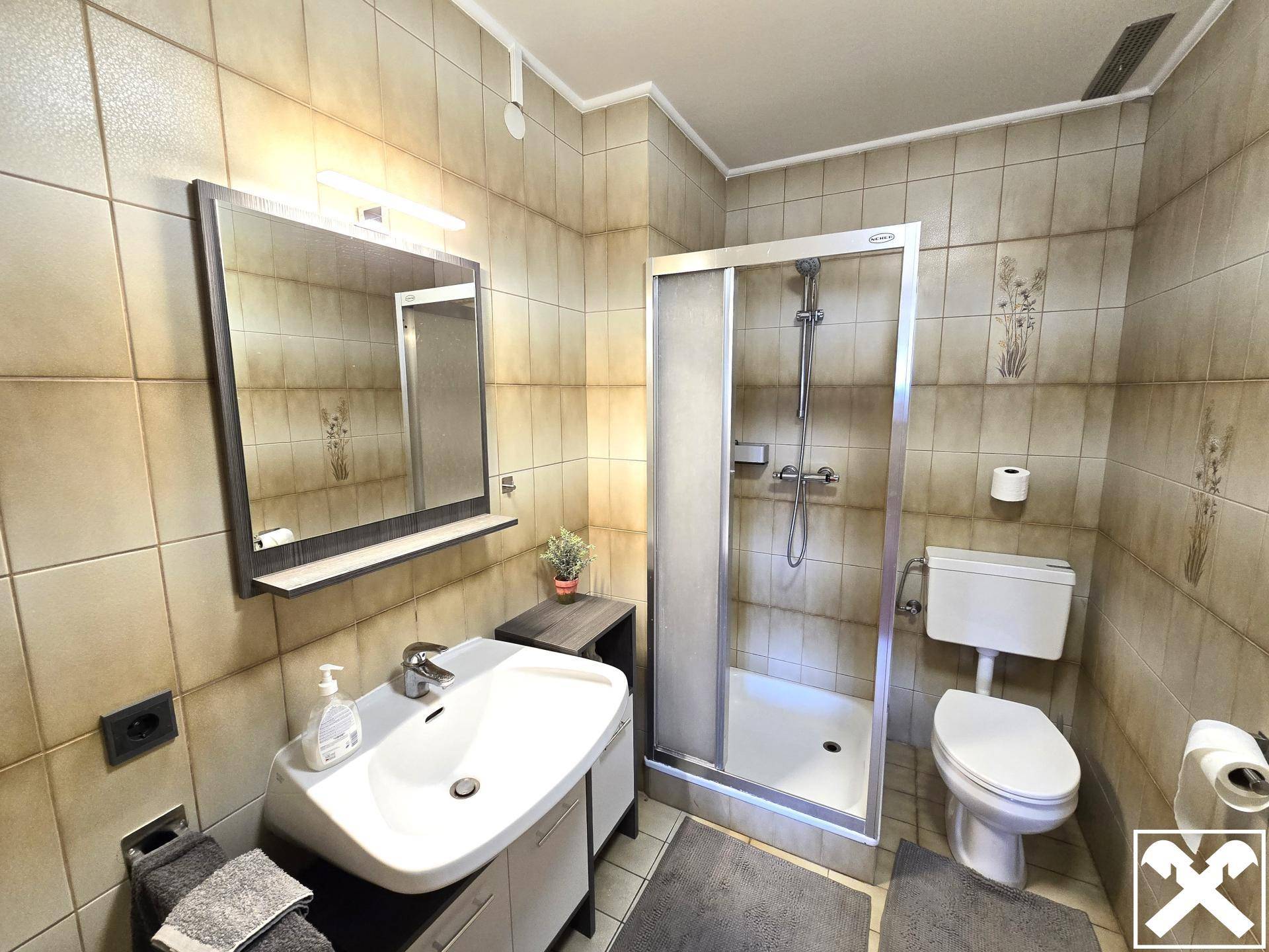 Funktionales Badezimmer mit beigefarbenen Fliesen, Duschkabine und Einzelwaschbecken.