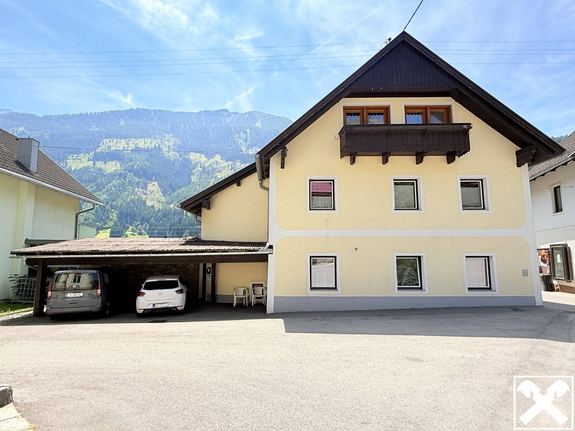 Seitenansicht des Hauses mit Carport für zwei Fahrzeuge und beeindruckendem Bergblick im Hintergrund.