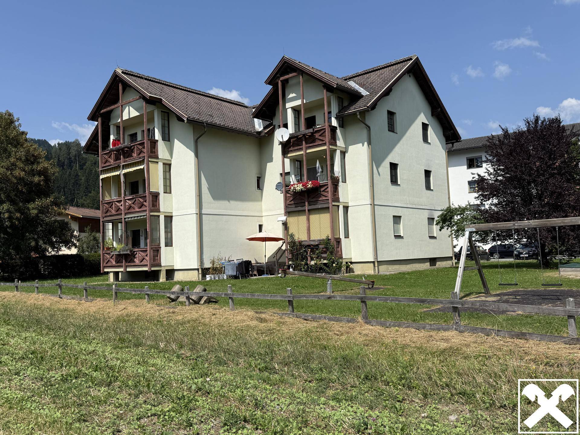 Mehrfamilienhaus mit mehreren Balkonen und einem kleinen Spielplatz im Grünen.