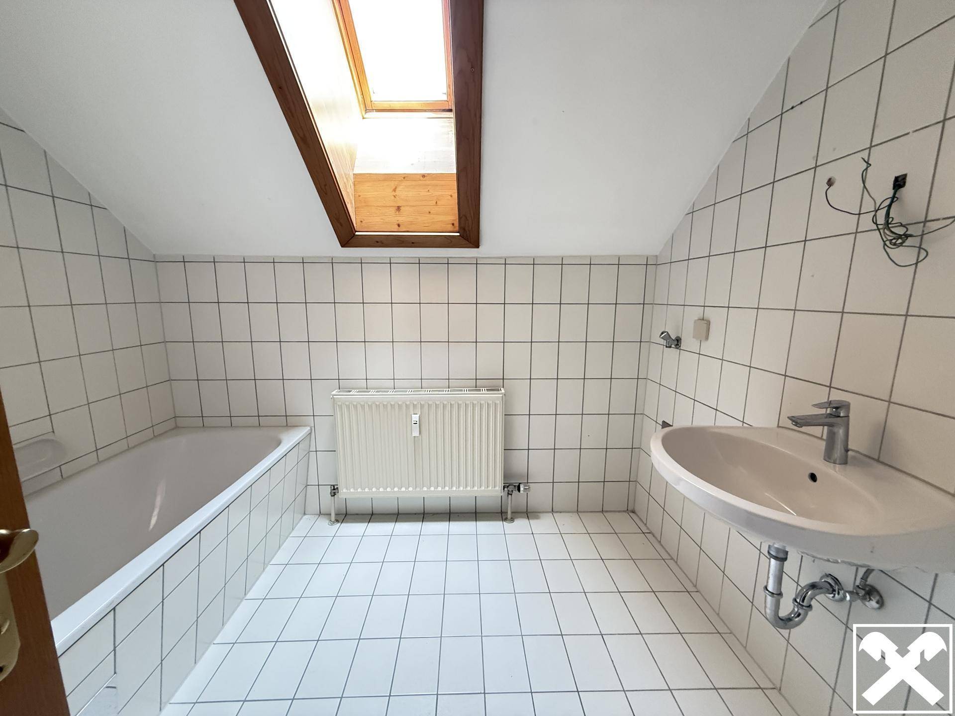 Badezimmer mit Badewanne, Waschbecken und Dachfenster, komplett gefliest in Weiß.