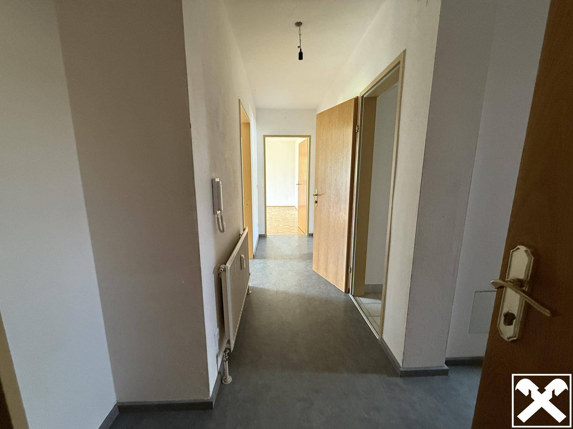 Heller Flur mit grauem Boden und weißen Wänden, der zu weiteren Räumen führt.