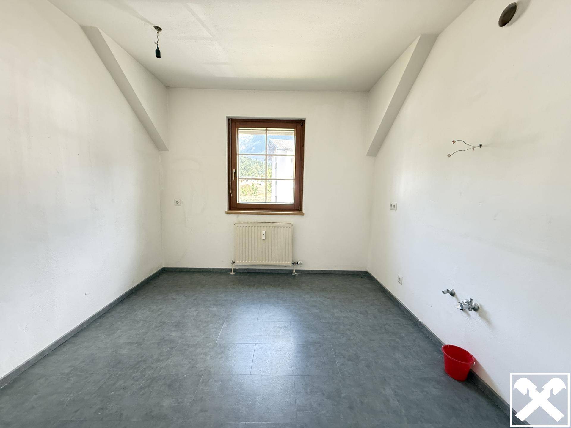 Funktionaler Raum mit grauem Fliesenboden und Fenster, vorbereitet für Installationen.