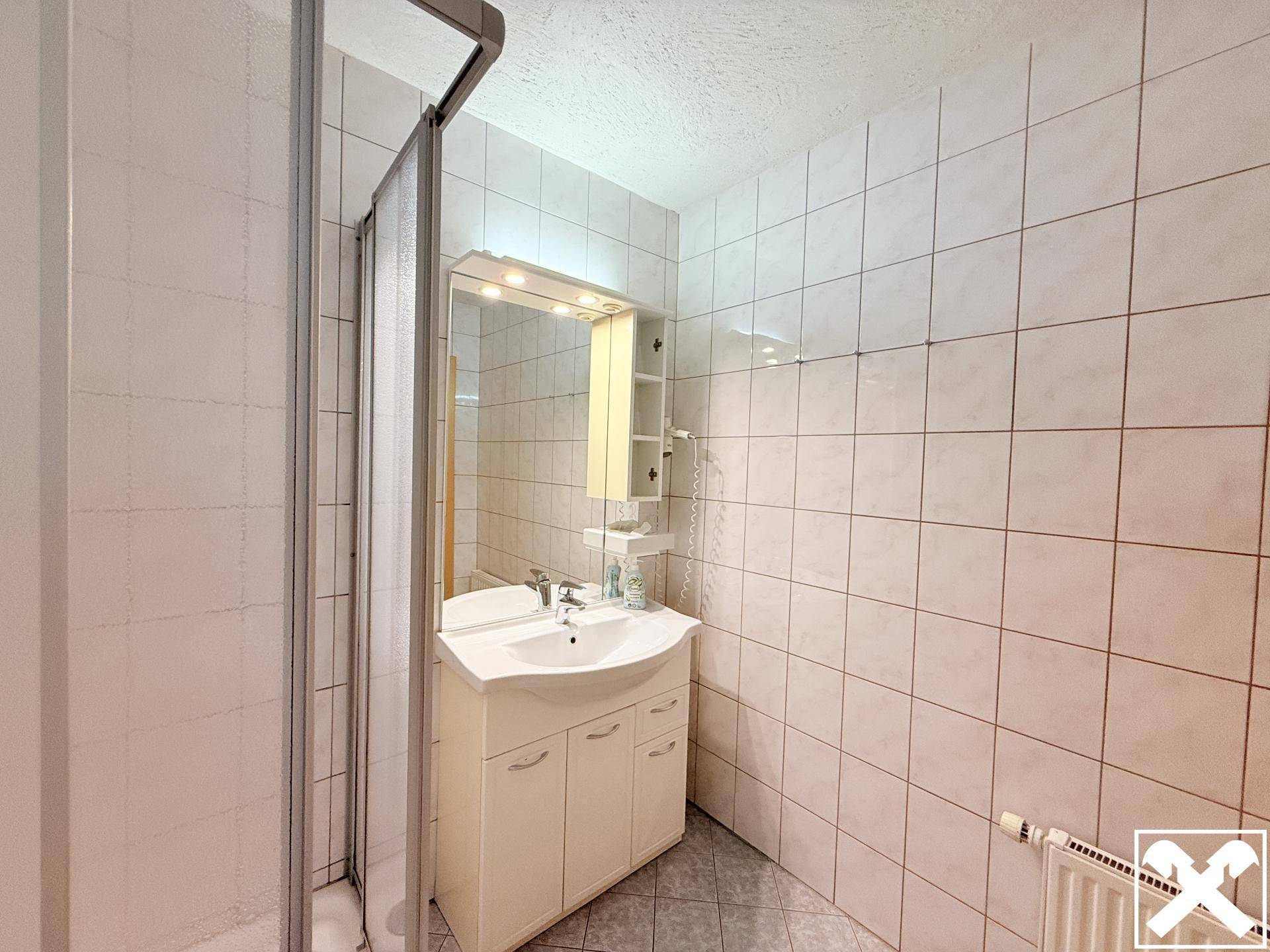 Funktionales Badezimmer mit Duschkabine, Waschbeckenunterschrank und weißen Fliesen an den Wänden.