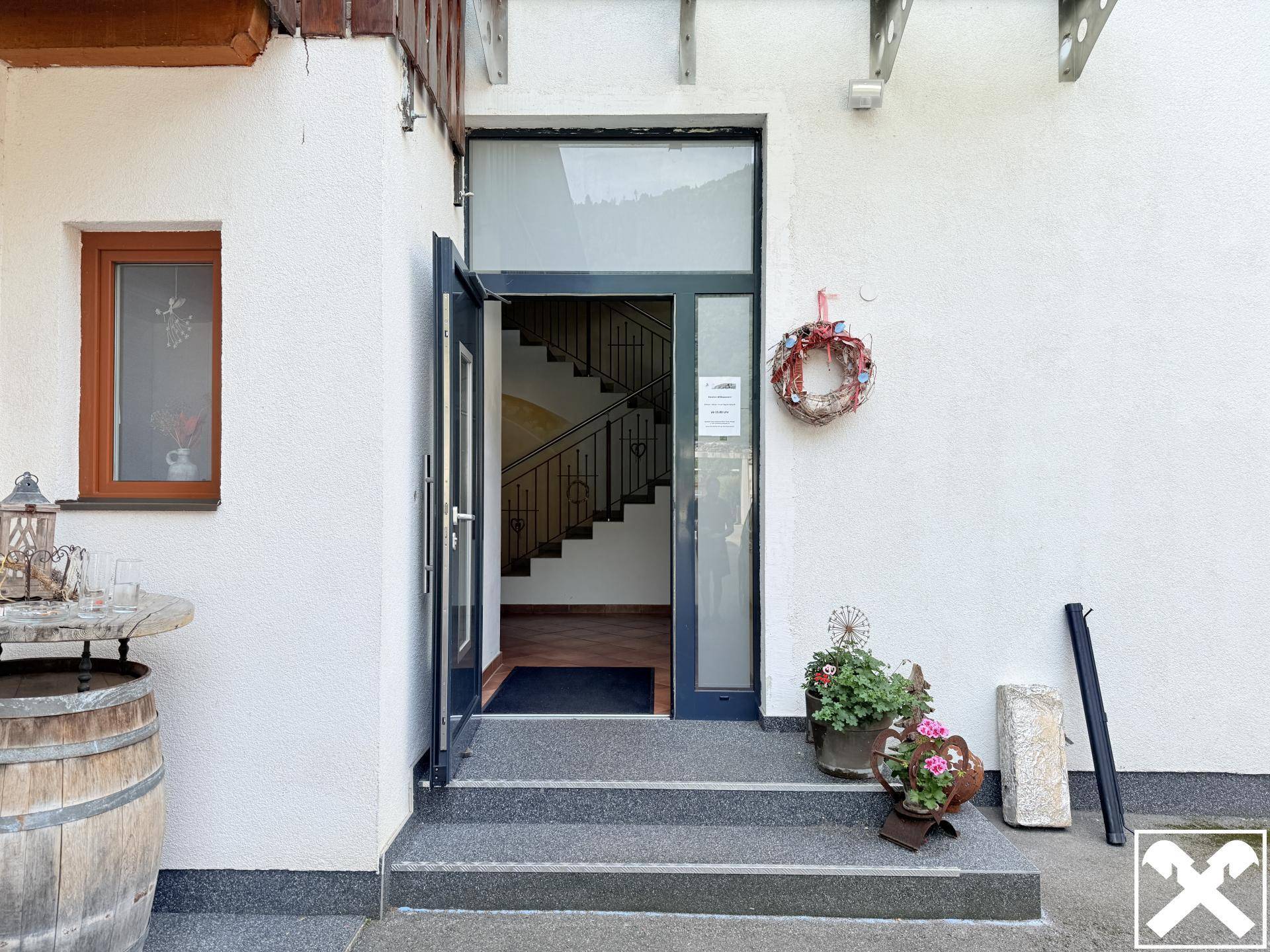 Eingangsbereich mit offener Tür, die eine Treppe im Inneren des Gebäudes sichtbar macht.