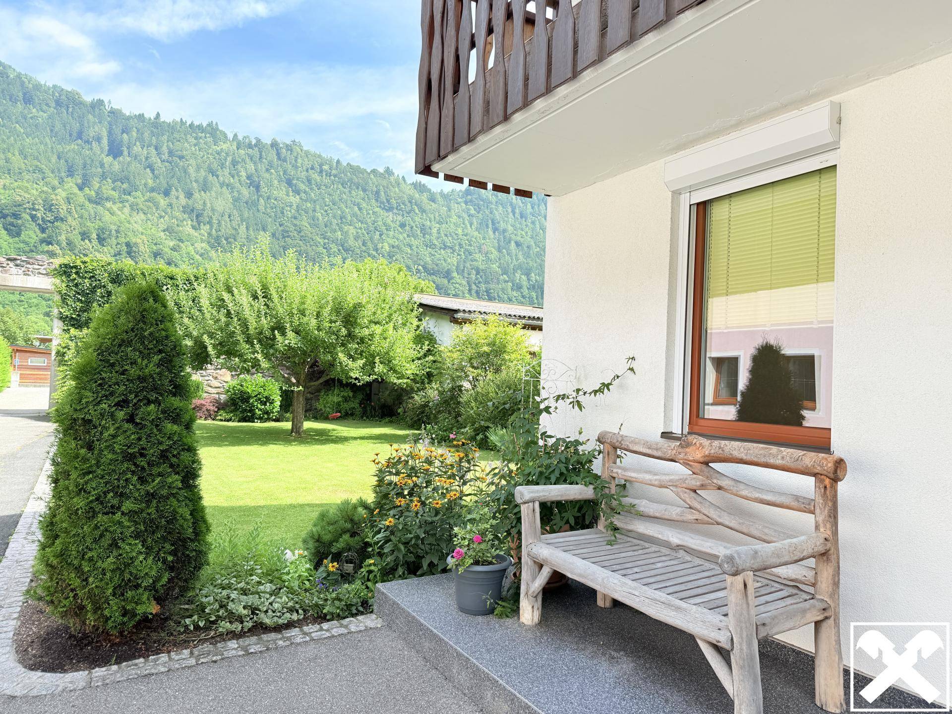 Gepflegter Gartenbereich mit Rasen, Bäumen und einer rustikalen Holzbank vor dem Haus.