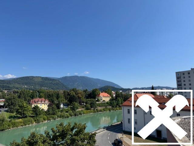 Weitläufiger Blick über einen Fluss, grüne Hügel und eine Stadtlandschaft unter klarem blauem Himmel.