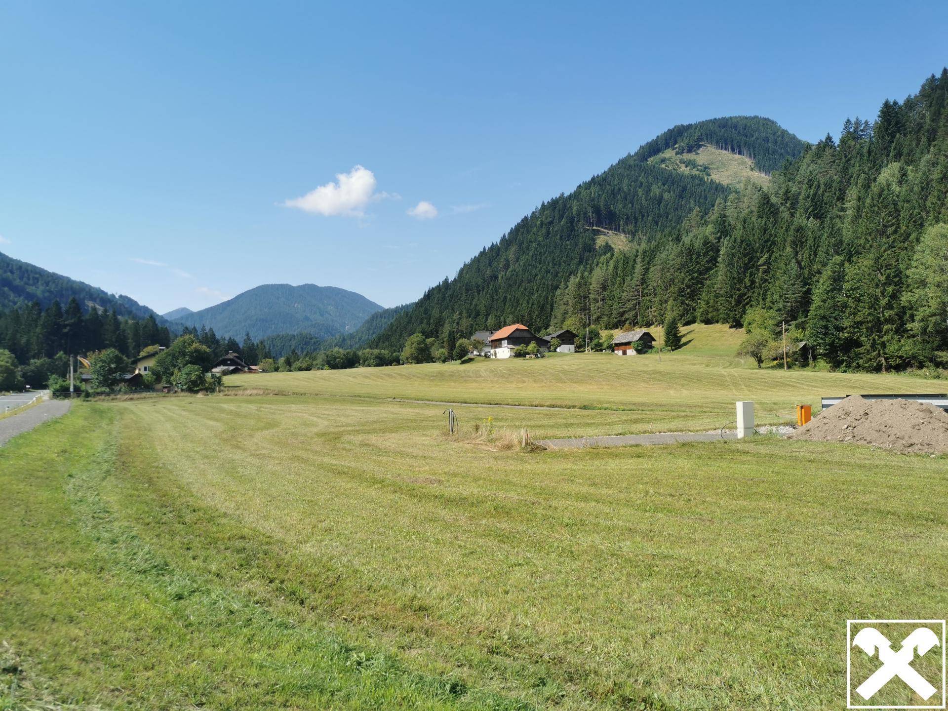 Panoramablick über weite grüne Felder und bewaldete Hügel, mit einigen Gebäuden im Tal und klarem Himmel.