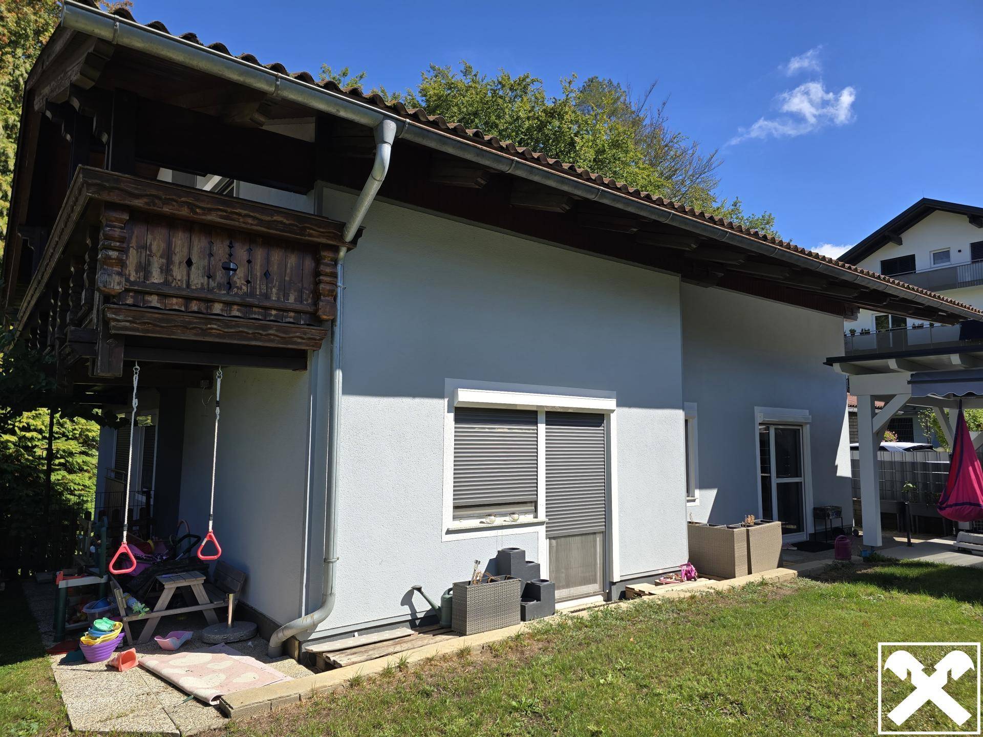 Seitliche Ansicht des Hauses mit Rasenfläche, Holzverkleidung und Kinderspielzeug im Garten.