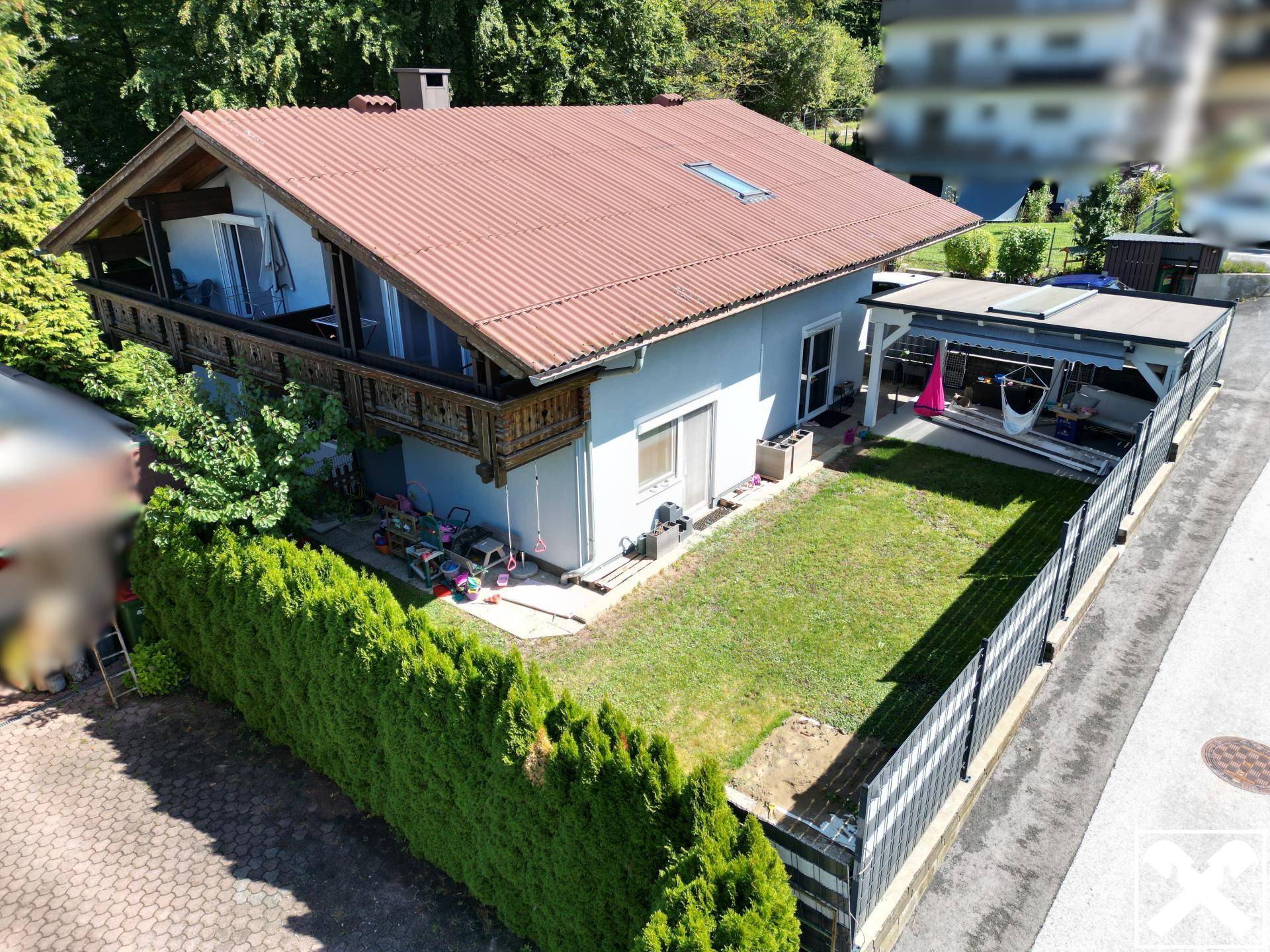 Luftaufnahme des Hauses mit seitlichem Holzbalkon, Rasenfläche und überdachtem Außenbereich.