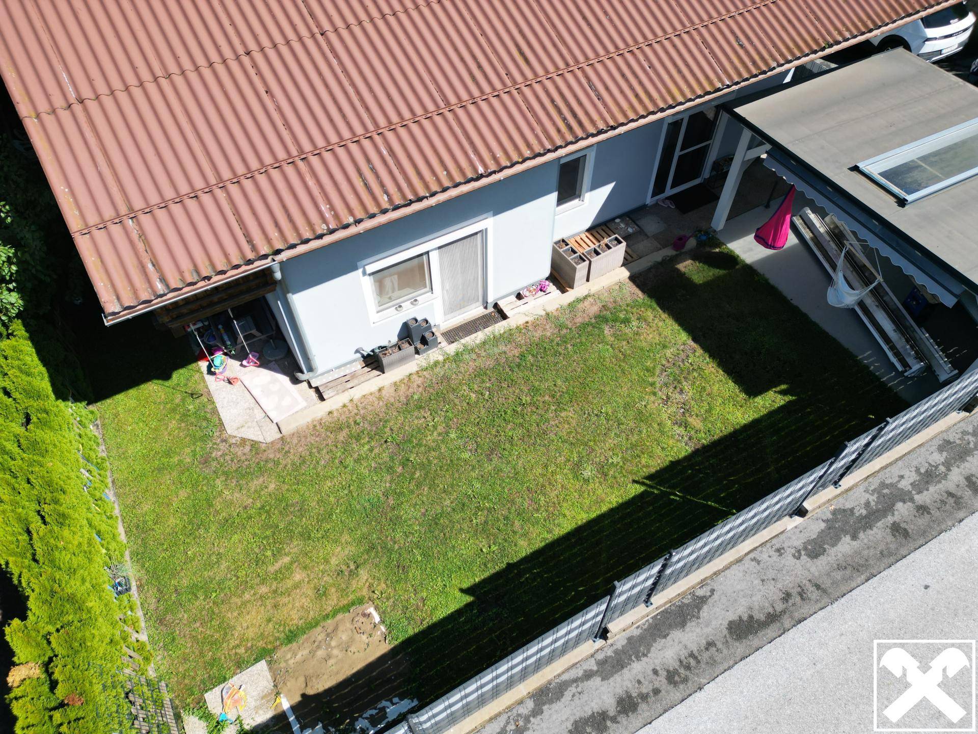 Blick von oben auf die kleine Rasenfläche neben dem Haus mit verschiedenen Gartenutensilien.