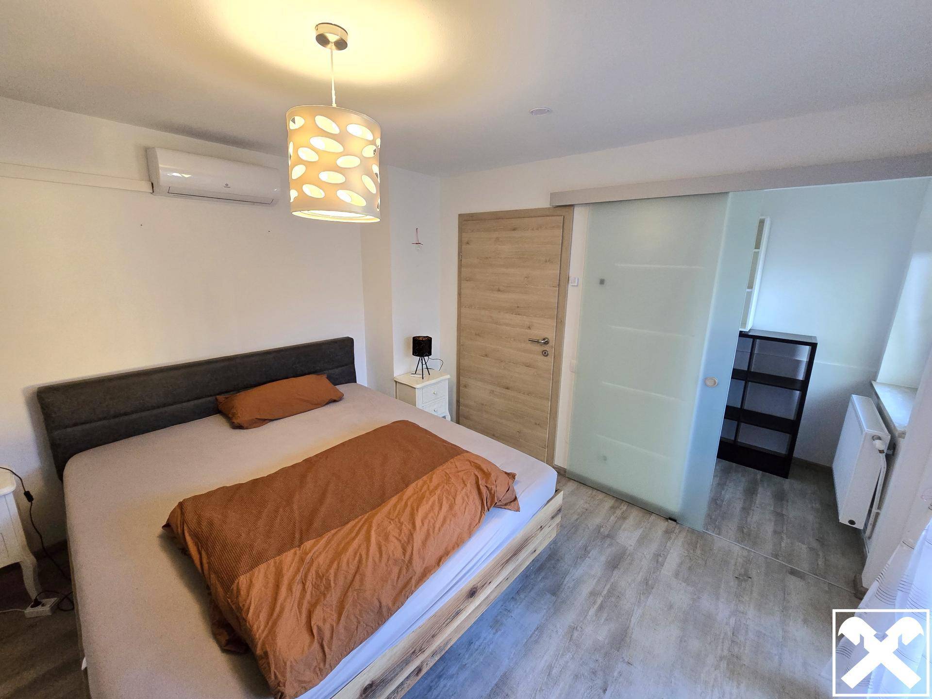 Schlafzimmer mit Doppelbett, Klimaanlage und Glasschiebetür zu einem Nebenraum.