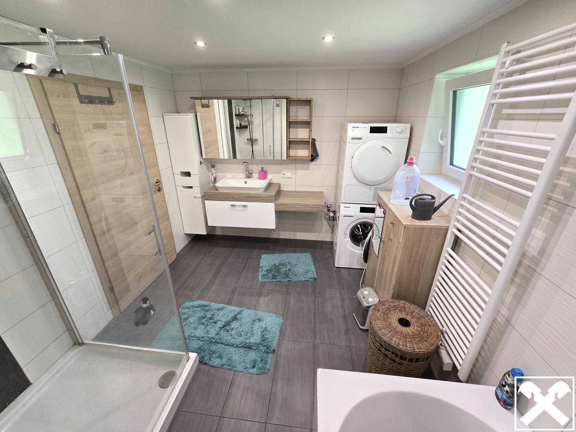 Badezimmer mit Waschtisch, Spiegelschrank, Waschmaschine, Trockner und Handtuchheizkörper.