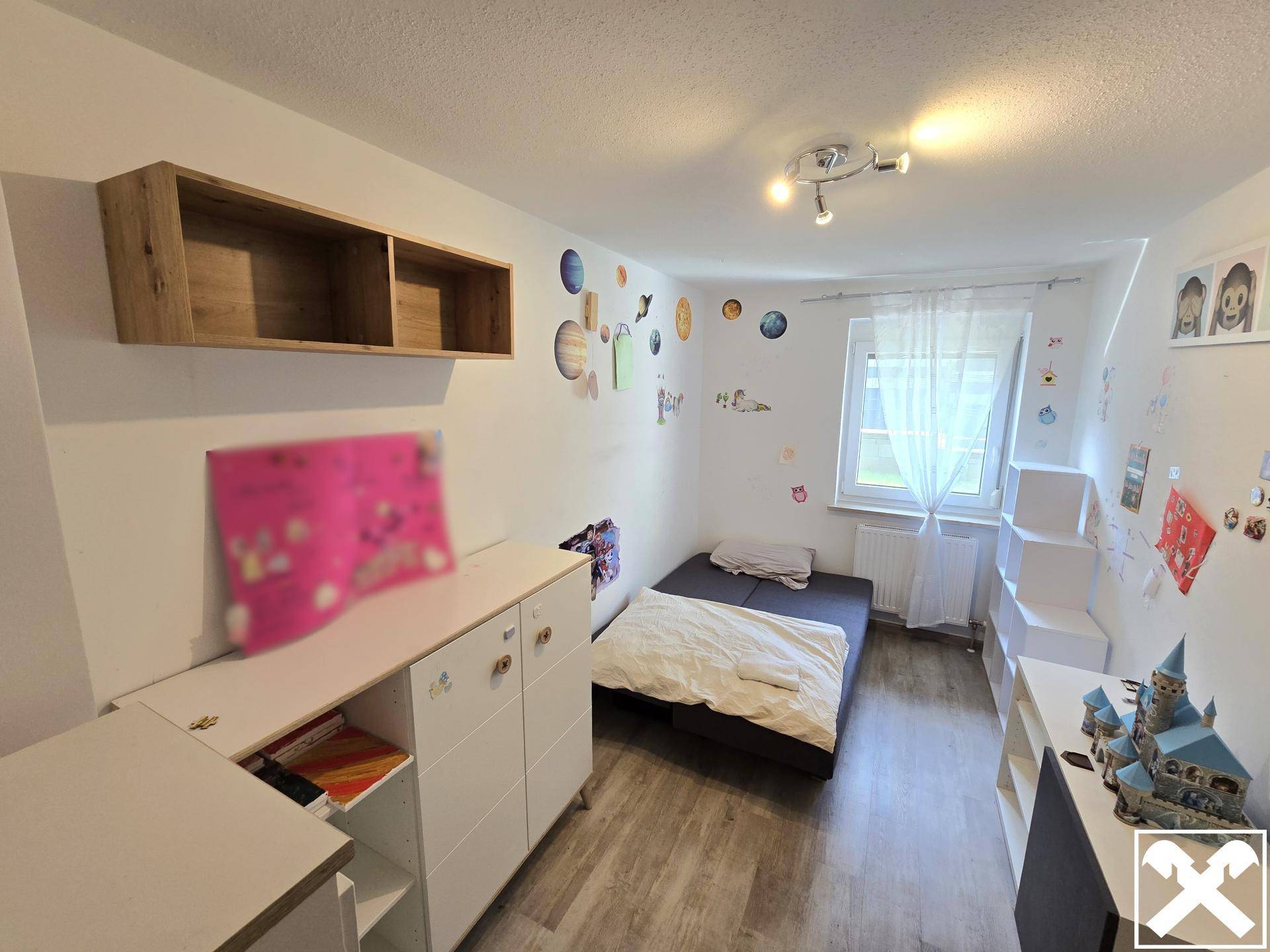 Kinderzimmer mit Einzelbett, Schreibtisch und farbenfrohen Wanddekorationen.