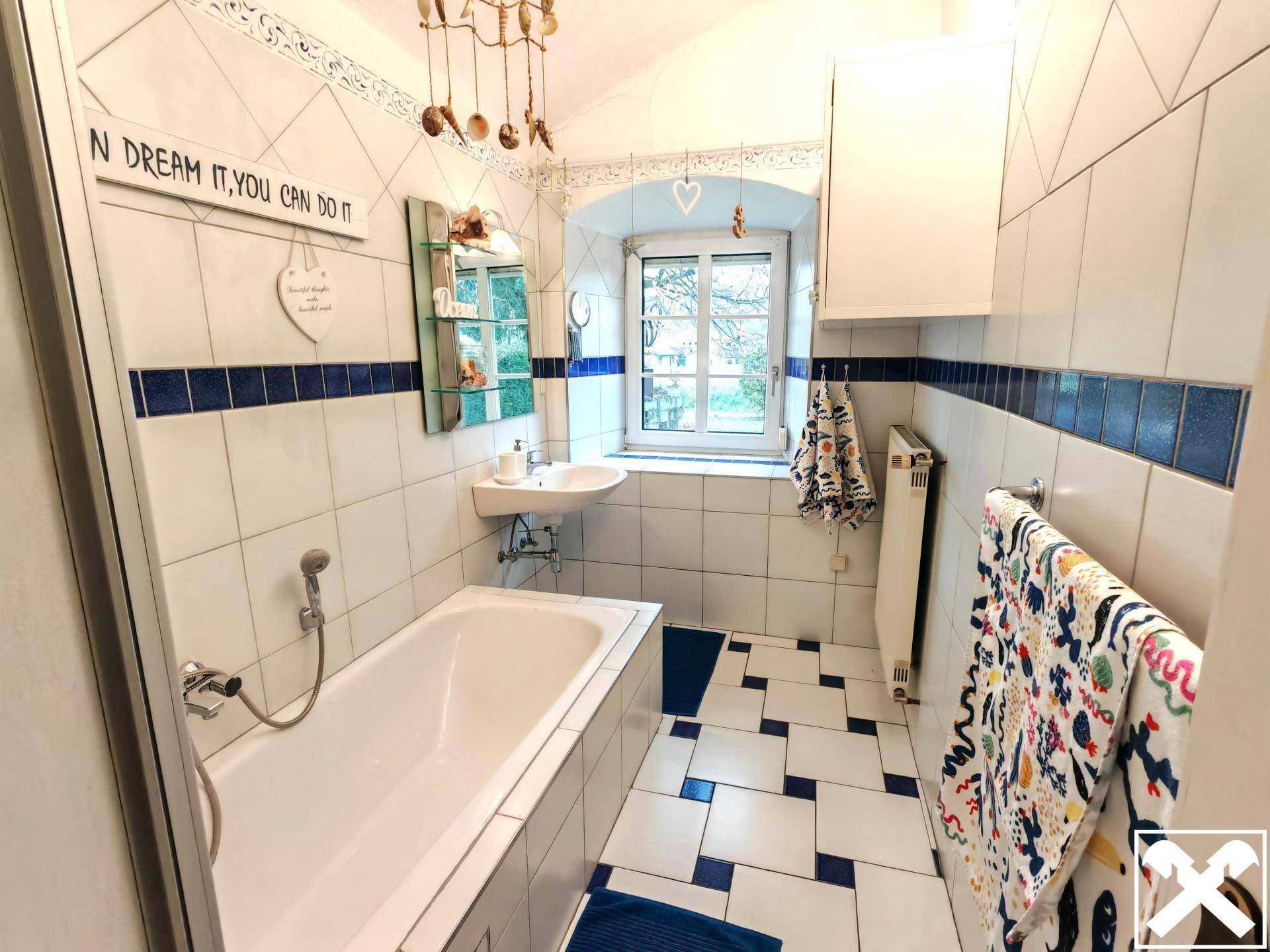 Helles Badezimmer mit Badewanne, Fliesen in Weiß und Blau sowie Fenster.